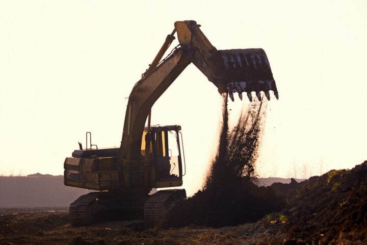 Bagger schüttet Erde auf Baustelle bei Sonnenuntergang